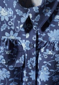 Navy blue floral shirt with light blue flower pattern, featuring a spread collar, two chest pockets, and button-down front. Textured fabric.