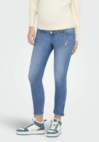 Jeans ajustados azules con un patrón desgastado, cremalleras en los tobillos y una cintura de media altura. Combinados con zapatillas altas azul y blanco.