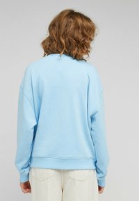 Sudadera azul claro con un corte relajado, cuello redondo y puños de canalé. Textura suave y dobladillo con costuras de hombro caídas.