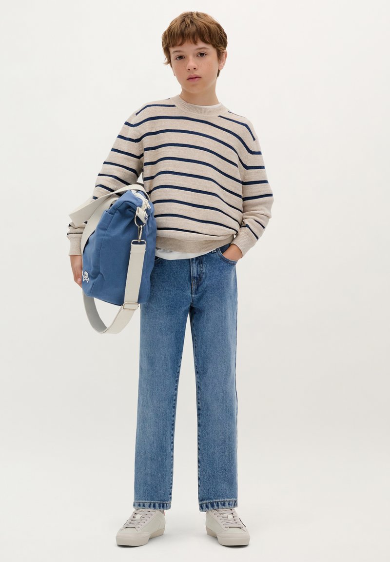 Blau- und cremefarbener gestreifter Pullover, lässige blaue Jeans und graue Sneaker. Blaue Tasche mit einem weißen Riemen und einem Schädelmotiv.