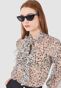 Blusa in tessuto trasparente con stampa leopardata, caratterizzata da dettagli a rouches, un fiocco al collo e una delicata palette di colori beige e grigio.