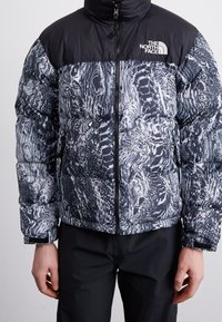 Dunjakke med en sort øverste sektion og en tekstureret grå og hvid mønstret nederste sektion. Lynlås og logo på brystet.