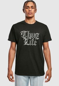 Juodas medvilninis marškinėlis su balta grafika, kurioje užrašyta "Thug Life". Marškinėliai turi trumpas rankoves ir apvalią iškirptę.