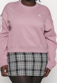 Ljusrosa sweatshirt med rund halsringning och vit tre-stripes design på ärmarna, i kombination med en svart och vit rutig minikjol.