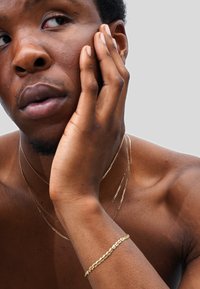 Gold jewelry includes multiple layered chains and a bracelet, set against bare skin. The texture is smooth, with a polished finish.