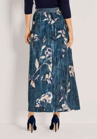 Maxi-jurk in een blauw bloemenpatroon, met een gesmokt tailleband en geplooide textuur. Geaccentueerd met tonale tinten en een vloeiende vorm.