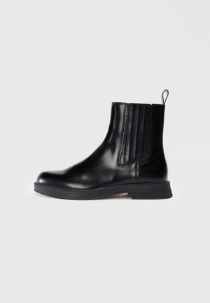 Bottine en cuir noir avec panneau latéral élastique, languette à l’arrière, bout arrondi et semelle en caoutchouc plate.
