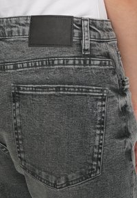 Närbild av en person som bär urtvättade svarta denimjeans som visar bakfickan och midjebandet med en svart läderlapp.