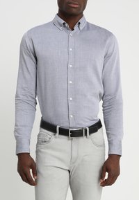 Camicia a maniche lunghe, con bottoni, in tessuto azzurro chiaro con una sottile texture, abbinata a jeans grigio chiaro e una cintura nera con accessori in argento.