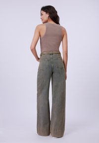 Brown ribbed tank top with wide leg, faded green denim pants. Pants feature two back pockets and braided belt detail. Smooth texture.