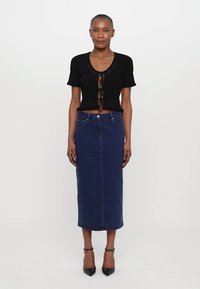Top scurt negru cu mânecă scurtă și detaliu cu funda în față, asortat cu o fustă midi din denim de culoare albastră închis. Are o formă ajustată și o siluetă clasică.