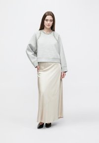 Sweatshirt cinzento com acabamento decorativo, mangas compridas e design cropped, combinado com uma saia maxi satinada creme lisa e sapatos pretos.