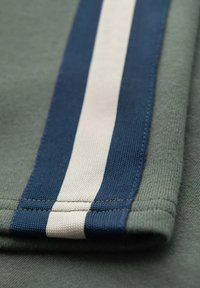 Tissu vert avec une texture côtelée présentant une bande bleu marine et une bande d'accent blanche. Les coutures sont visibles et bien finies.