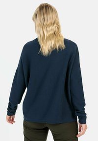Navyblauwe oversized trui met geribbelde textuur, drop shoulders en lange mouwen, gecombineerd met olijfgroene broek.