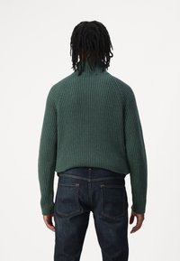 Maglione righe scure con collo alto e maniche raglan, abbinato a jeans scuri, mostrato da dietro. Dettaglio del tessuto testurizzato visibile.