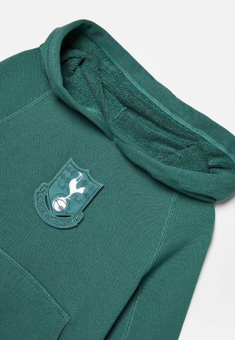 Hoodie vert avec un patch du logo de Tottenham Hotspur sur la poitrine, mettant en avant un coq et un design de blason, posé à plat sur un fond blanc.