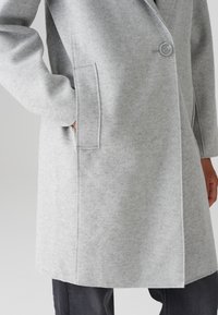 Grijze wolmix jas met een enkele knoopsluiting, zijzakken en een gladde textuur. Beschikt over een getailleerde pasvorm en minimale stikseldetails.