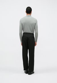 Gaiši pelēks pieguļošs krekls ar garām piedurknēm, kombinēts ar melniem pielāgotiem biksēm, kurām ir taisna griezuma forma, un spīdīgām melnām kurpēm.