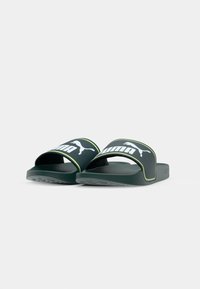 Sandales en plastique noires et vertes avec une large sangle présentant un logo blanc, un semelle texturée et une semelle plate et durable.
