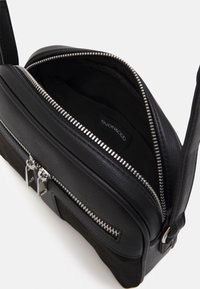 Borsa a tracolla in pelle nera con apertura zip, hardware in argento e design testurizzato. L'interno è foderato in tessuto e presenta un'etichetta con logo.