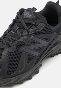 Schwarzer Sportschuh mit einem Mesh-Obermaterial, gepolstertem Sohlen, auffälligem Logo, strukturierten Akzenten und robustem Profil für besseren Halt.