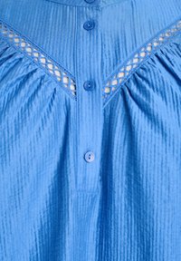 Blue button-up shirt with textured fabric, featuring a crinkled design and lace accents at the neckline. Four buttons visible.