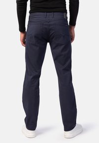 Marineblaue Baumwollhosen mit geradem Bein, ausgestattet mit zwei Gesäßtaschen und minimalen Nähdetails, kombiniert mit weißen Sneakern.