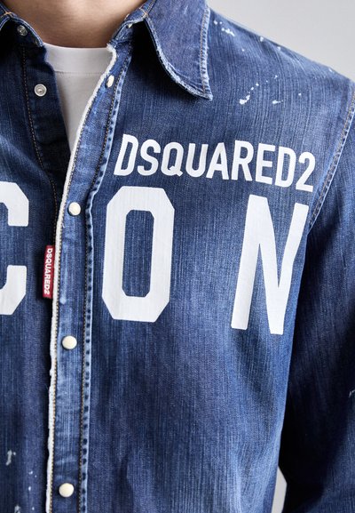 Tumesinine denim-paita, millel on kaks suurt valget tähte "C" ja "N" ning "DSQUARED2" bränding ees. Olemas on kulunud aktsendid.