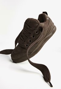 Rjave športne čevlje z teksturiranim površjem, okroglimi vezalkami in oblazinjenim ovratnikom. Imajo gumijast podplat in perforirane detajle na konici.