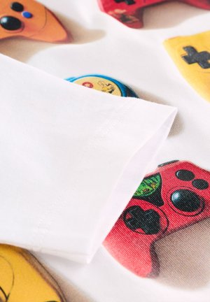 Weißer Stoff mit bunten Spielkontroller-Motiven in Orange, Gelb, Rot und Blau. Feine Nähte sind am Ärmelsaum sichtbar.