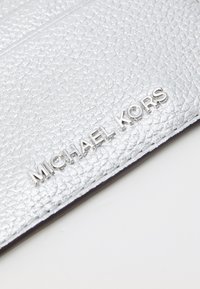 Zilveren leren portemonnee met een gegraveerd "MICHAEL KORS"-logo in glanzend zilveren hardware. Heeft een textuur oppervlak en strakke randen.