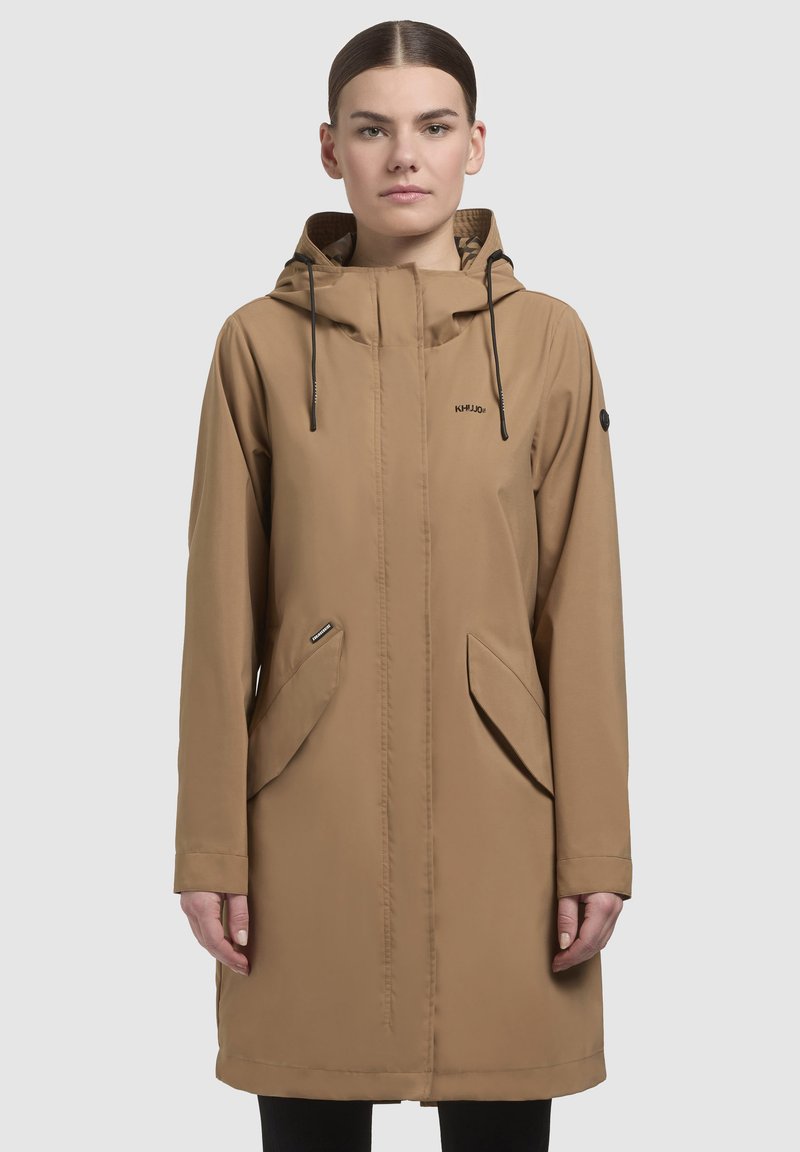 Bež vodootporna jakna s kapuljačom, zippered džepovima i čistim dizajnom. Ima čipke i logo na prsima. Glatka tekstura.