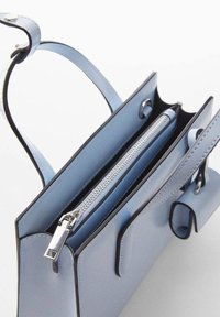 Bolso de mano de cuero azul con bordes negros, con un asa superior, compartimento principal con cremallera y solapa decorativa. Textura suave y diseño minimalista.