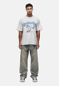 Lichtgrijze oversized t-shirt met blauwe vlinderafbeeldingen, gecombineerd met losse vervaagde denim jeans en zwart-witte sneakers.