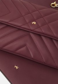 Vinjettläderclutch med kviltad chevrondesign, med guldfärgade detaljer och logotypackenter. Slät textur med noggrant sydda sömmar.