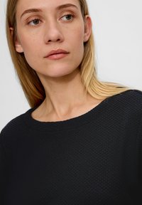 Zwart gebreid sweater met een ronde hals, voorzien van een subtiel patroon. De stof lijkt zacht, met een losse pasvorm en een gladde afwerking.