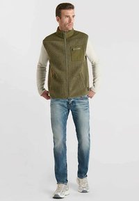 Grüne Fleece-Weste für Herren mit Reißverschluss und Brusttasche, kombiniert mit hellblauen Jeans und grauen Turnschuhen. Weiche Textur, sportliches Design.