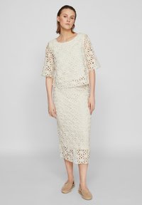 Spissstrikket to-dels antrekk i off-white, med en løs topp med trekvart ermer og et knelangt skjørt. Myk tekstur og blomstermønster.