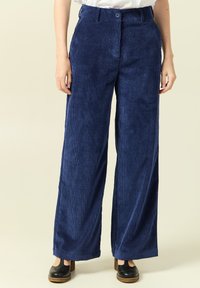 Mörkblå kordflossbyxor med vida ben, vertikala ränder, knappstängning och avslappnad passform. Har en mjuk textur och är hel-långa.