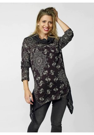 Sort tunika med intrikate hvide paisley- og mandala-mønstre, lange ermer, en draperet hals og asymmetrisk kant med blonde detaljer.