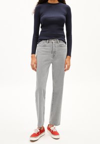 Granatowa, prążkowana bluzka z długim rękawem, szare dżinsy o wysokim stanie i prostych nogawkach oraz czerwone, płócienne trampki z białą podeszwą. Prosty i casualowy strój.