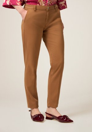 Pantaloni slim-fit marroni realizzati in tessuto liscio, dotati di passanti per cintura, tasche laterali e design a gamba dritta. Indossati con ballerine in vernice borgogna.