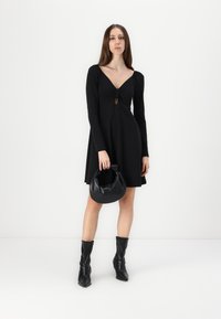 Vestido preto de mangas compridas com um profundo decote em V e detalhe em forma de buraco, combinado com uma bolsa redonda preta e botas de couro até aos joelhos.