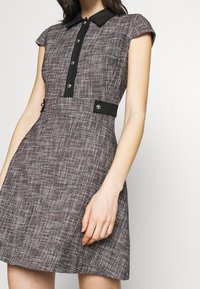 Sukienka z krótkim rękawem z fakturowanej czarno-białej tkaniny. Posiada czarny kołnierz, zapięcie na guziki z przodu oraz akcenty w talii z srebrnymi elementami.