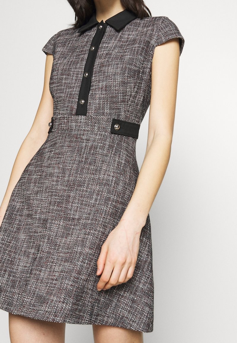 Sukienka z krótkim rękawem z fakturowanej czarno-białej tkaniny. Posiada czarny kołnierz, zapięcie na guziki z przodu oraz akcenty w talii z srebrnymi elementami.