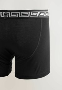 Schwarze Baumwoll-Boxershorts mit glatter Textur, ausgestattet mit einem gemusterten elastischen Bund in Silber und Schwarz.