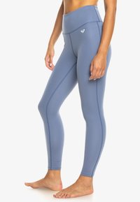 Leggings taille haute en matériau doux et bleu clair avec une texture lisse. Présente des coutures discrètes et un petit logo sur la taille.