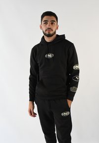 Conjunto de sudadera y pantalones de chándal negros, hecho de tela suave, con detalles de logo en el pecho y las mangas, corte holgado y cintura con cordón.
