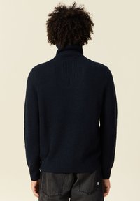 Sweater en maille côtelée bleu marine avec un col montant, présentant des manches longues et une coupe décontractée, montré de dos sur un fond clair.