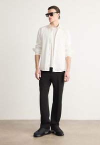 Baltas marškiniai su apykakle ant paprasto balto marškinėlio, juodos kelnės ir juodi sportbačiai. Papuošta didelėmis juodomis saulės akimis.